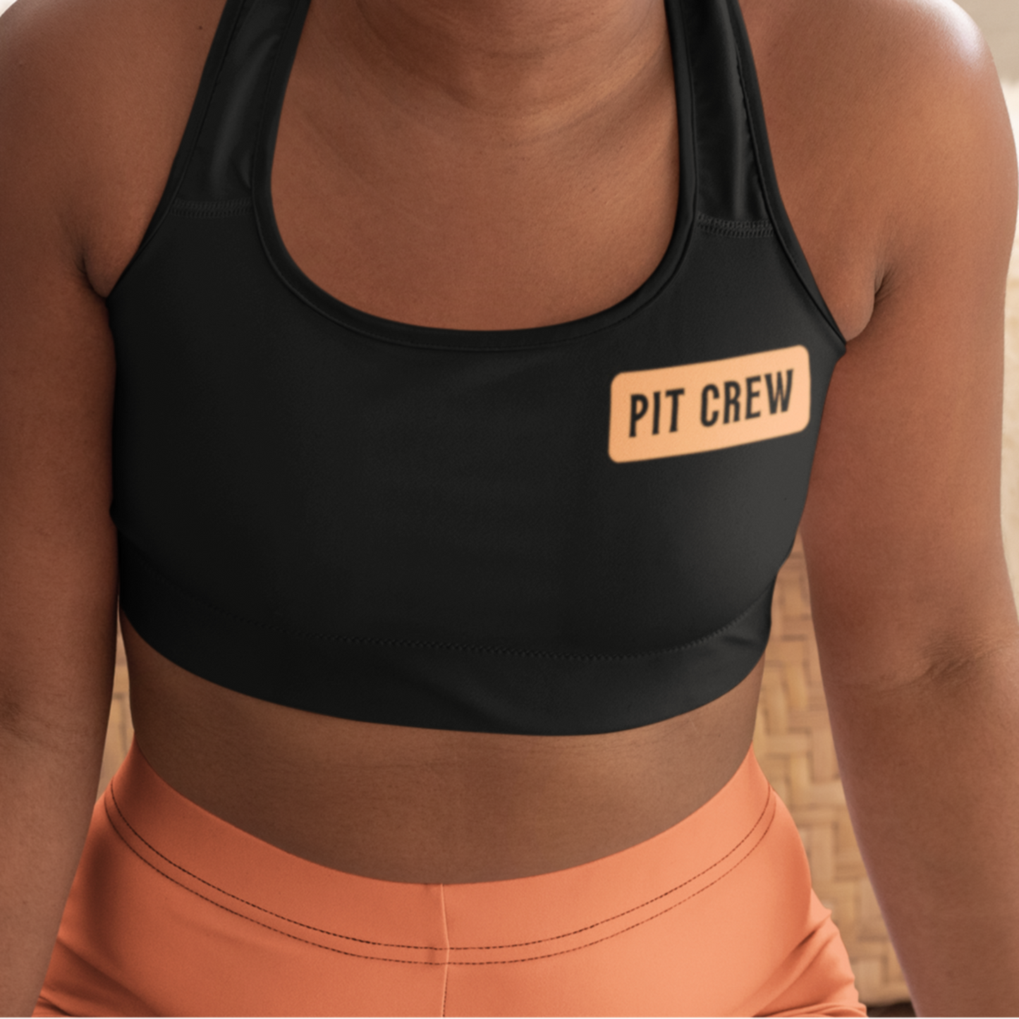 Black sports bra with 'PIT CREW' patch worn by a person, against a neutral background.
