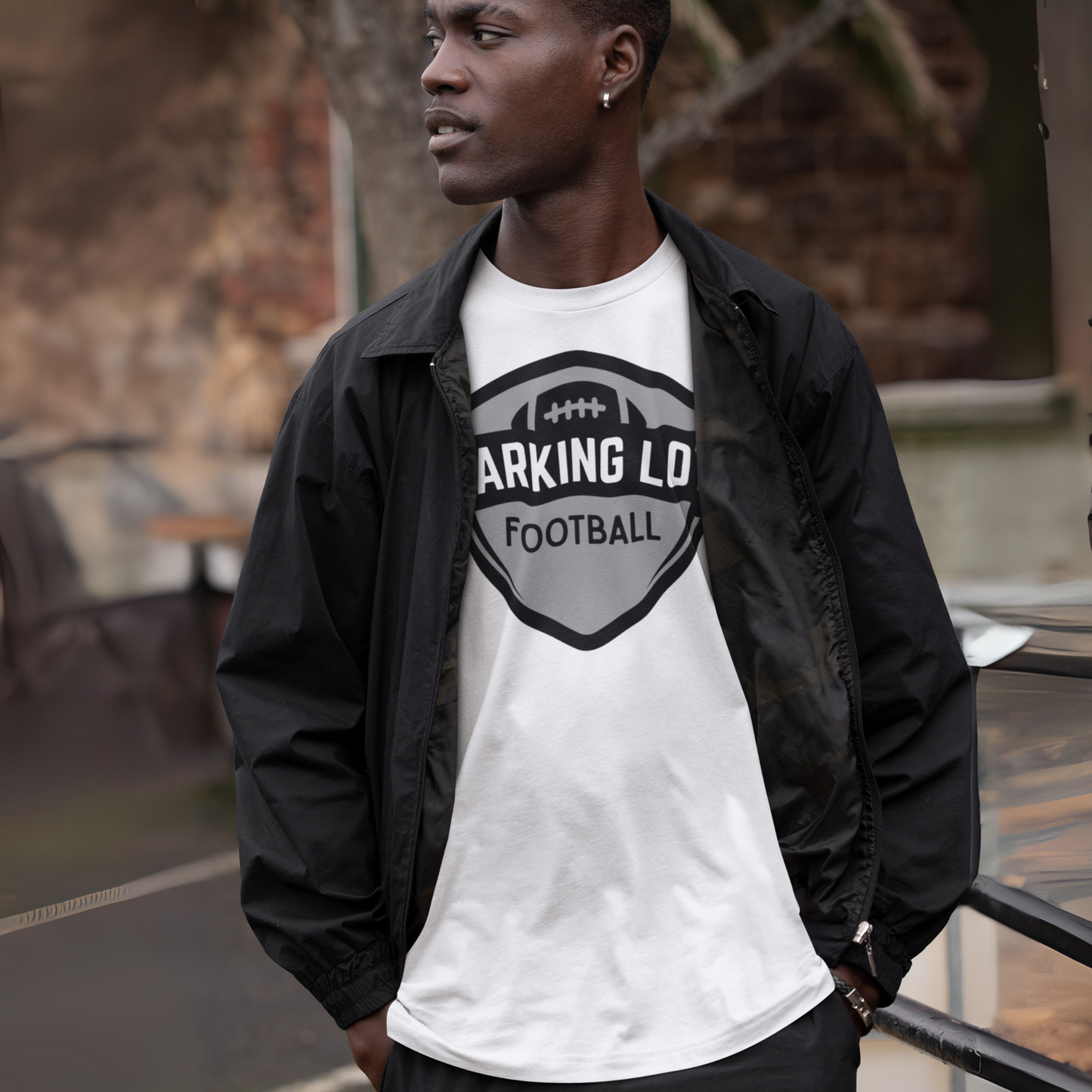 Person wearing a white t-shirt with 'PARKING LOT FOOTBALL' text and black jacket outdoors.