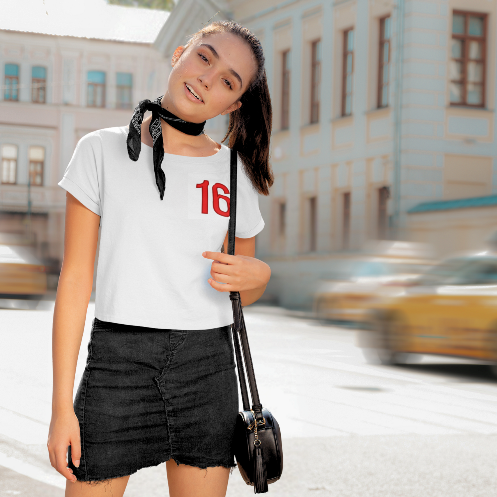 Woman in a city street wearing a white t-shirt with the number 16 and black skirt.