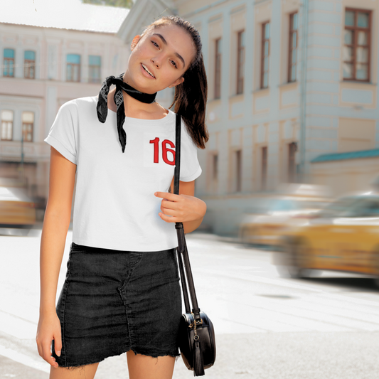 Woman in a city street wearing a white t-shirt with the number 16 and black skirt.