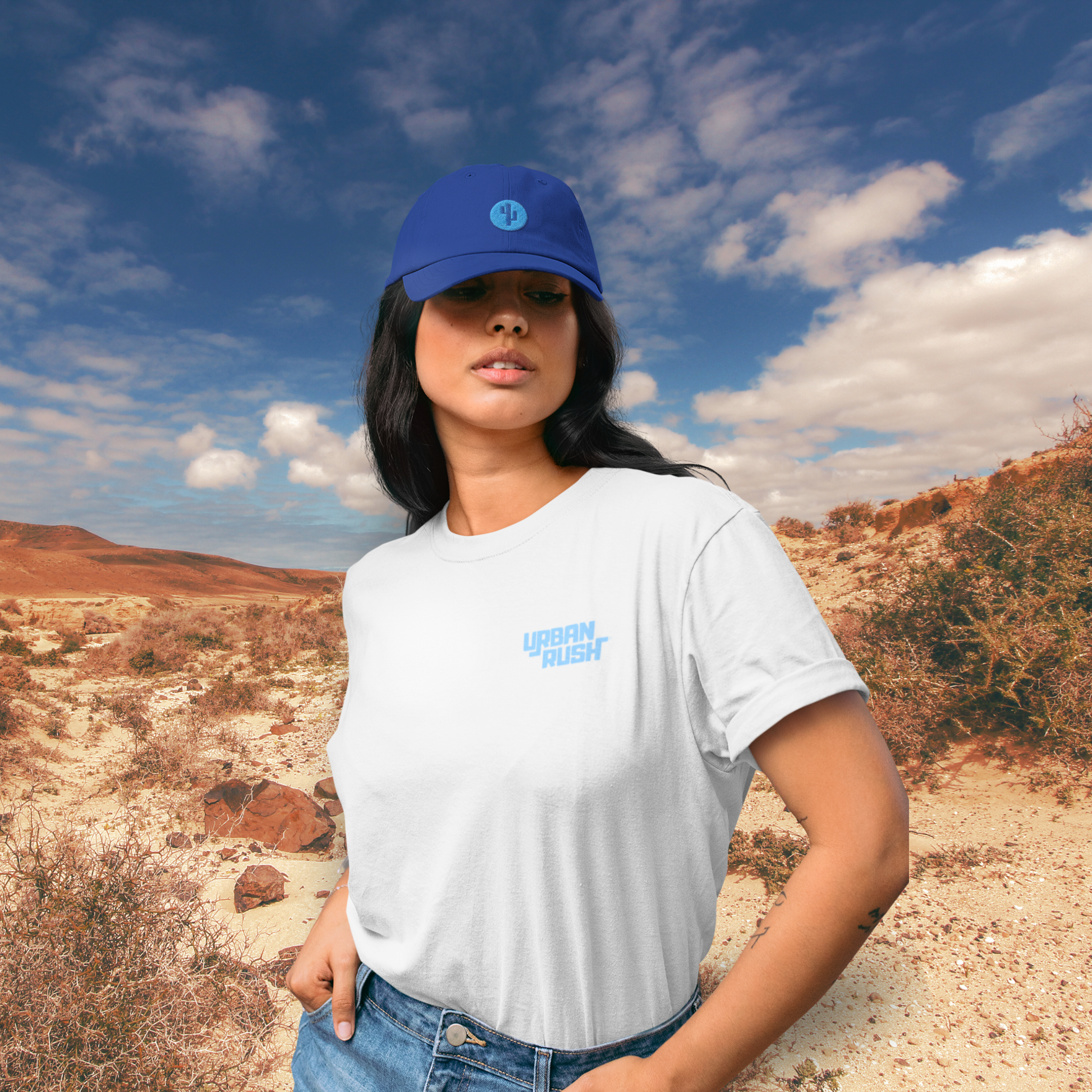 Model wearing a blue hat, standing in a desert landscape.