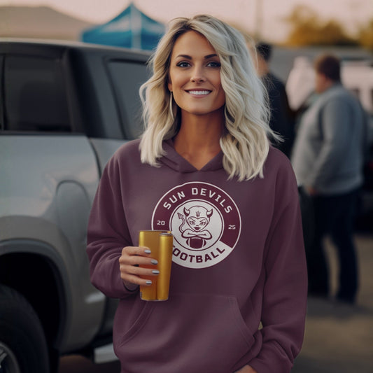 Woman wearing a maroon hoodie with a 'Sun Devils Football' logo, holding a drink, standing in a casual outdoor setting.