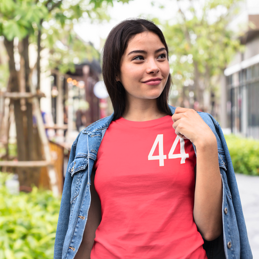 A natural and stylish model, in a bright red Quali Day tee featuring the number '44' in Urban Rush Originals Women's 44 Quali Day Relaxed Soft Tee in Red, worn by a young woman with dark hair and a denim jacket in a bright outdoor setting, showcasing the relaxed fit and bold '44' graphic.