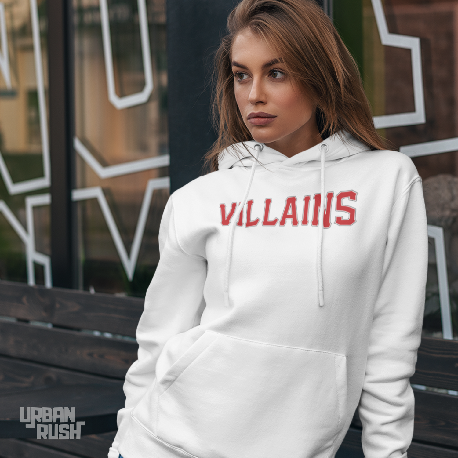 Woman wearing a white hoodie with 'VILLAINS' in red text, leaning on a bench.